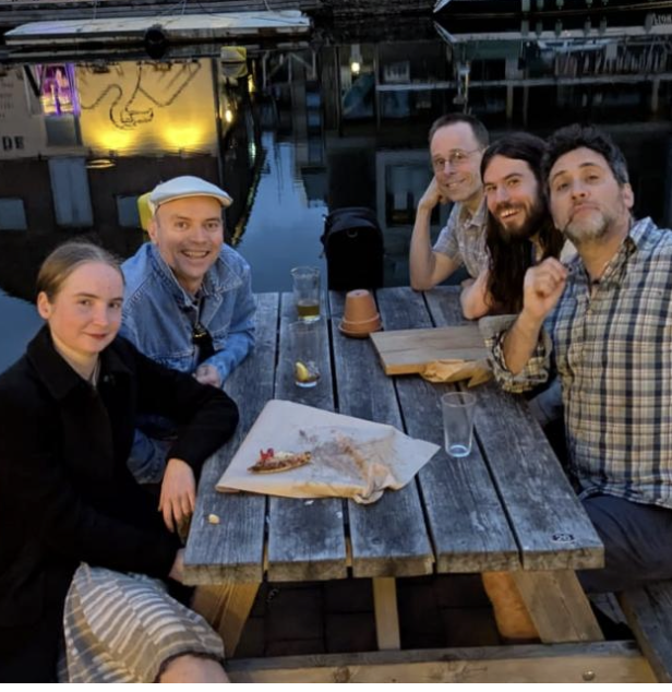 K-House musicians gathered around an outdoor table by the water in Exeter